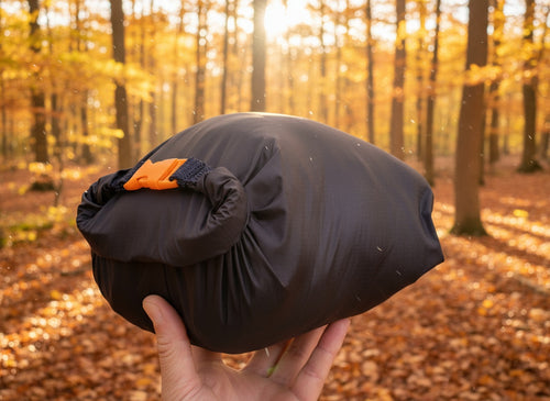 Person holding a packable dog bed  in a forest during sunset.
