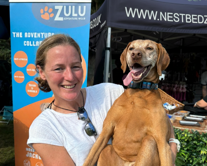 Woman holding a dog with a ZULU banner and NestBedz tent in the background
